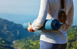 Woman standing on a mountain with her yoga mat in hand